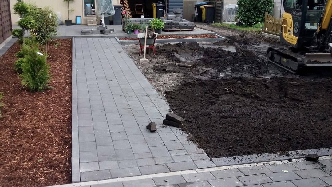 Neu gepflasterter Gehweg neben einem in Arbeit befindlichen Gartenbereich.